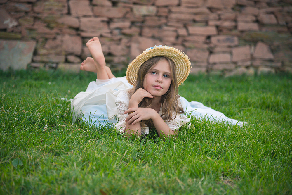 Fotografías de Su Primera Comunión de una niña con su vestido y un sombrero de paja en un parque en exterior en Madrid, cerca de Pozuelo de Alarcón.